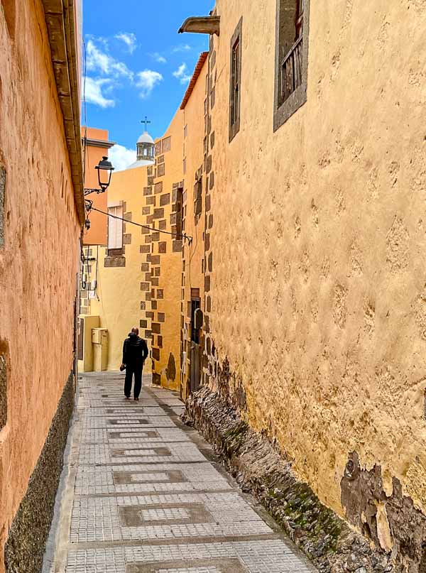 man walking down narrow street in a colonial town under a blue sky