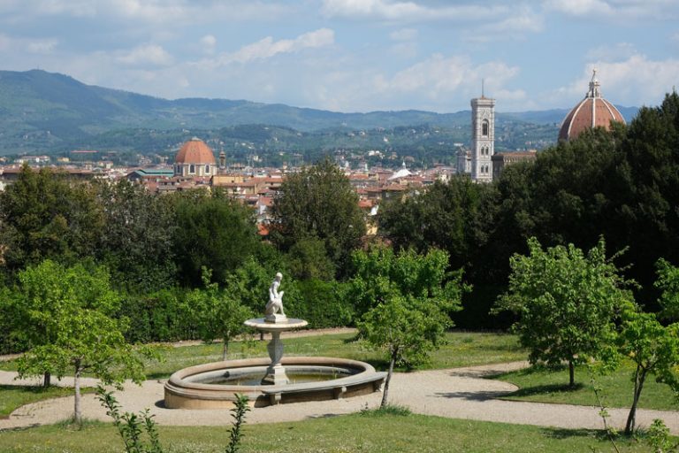 formal garden with small tress and a central fountain and views over florence