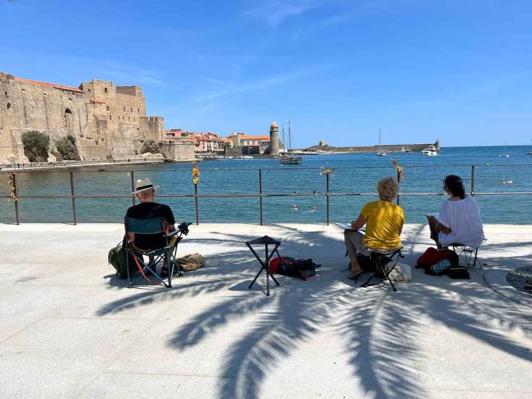 three people sitting by the seafront painting an old castle in collioure france