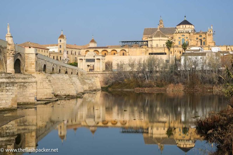 reflection of the mezquita of cordoba in still river with arched stone bridge