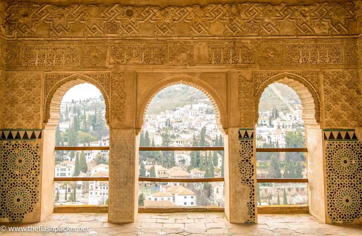 three beautifully carved islamic arches providing views of houses on hillside