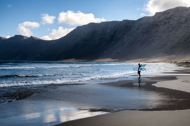 man with a surf board walking along a beach