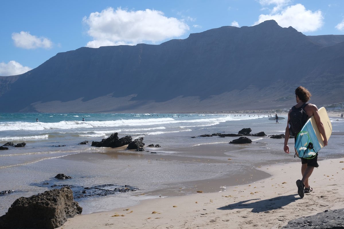 man walkoing along a sandy beach with a surfboard