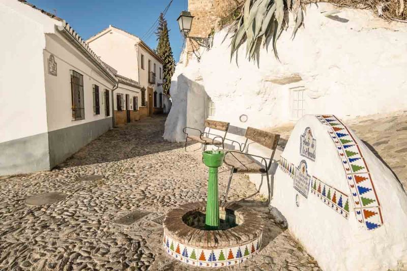 small green fountain on a cobblestone street with whitewashed low buildings in granada spain