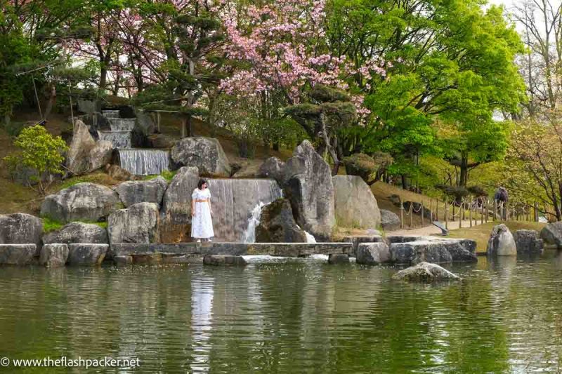 woman in white dress standing by waterfall