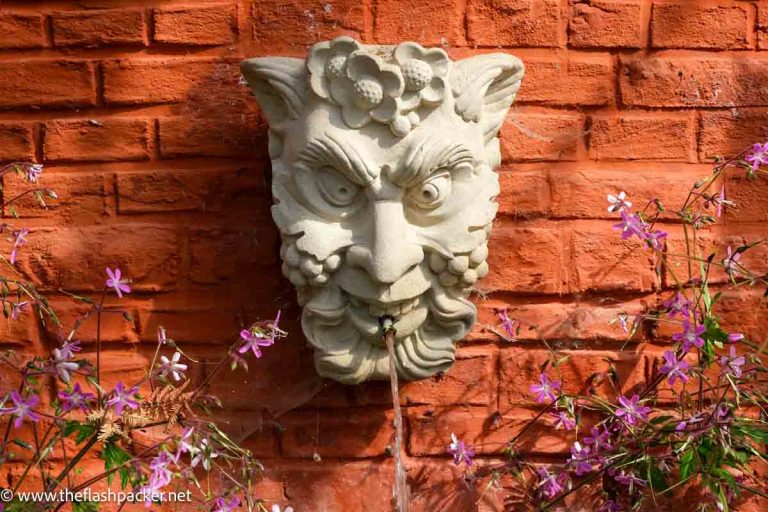 stone fountain of face of satyr against a terracotta wall at leuven botanical garden