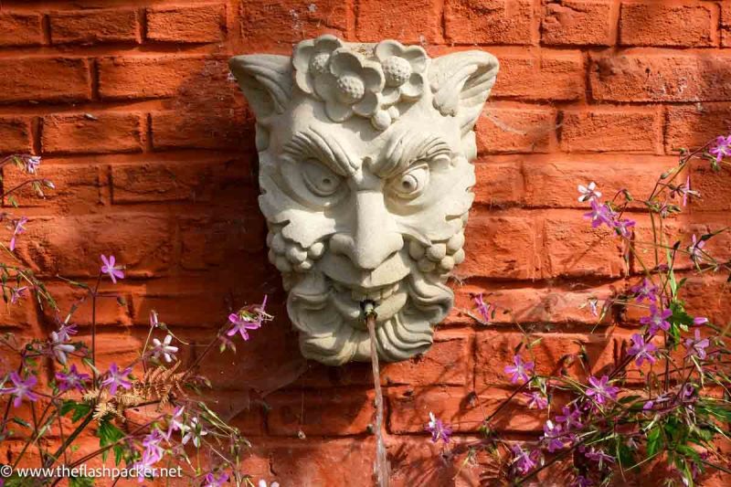 stone fountain of face of satyr against a terracotta wall at leuven botanical garden