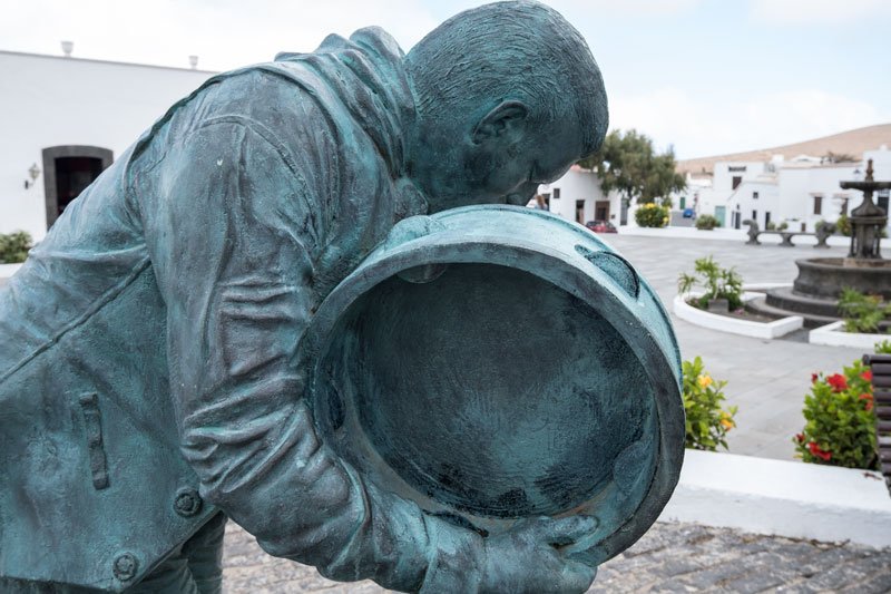 bronze sculpture of a man playing a tambourine in a colonial square lined with low whitewashed buildings in teguise in lanzarote