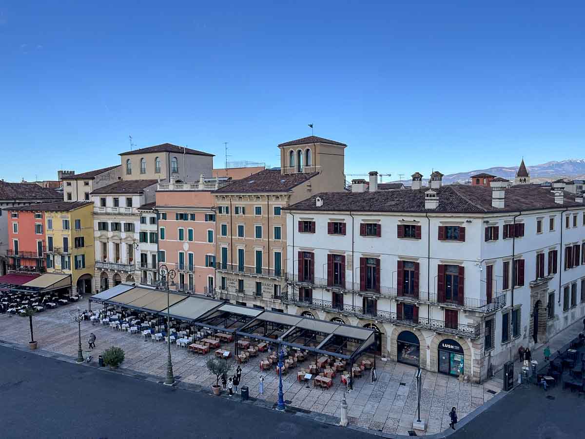 tables and chairs in front of row of pastel-coloured medieval buildings in piazza bra in verona italy