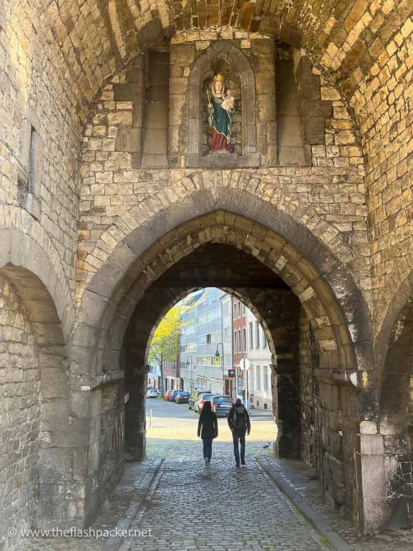 two people walking through the arch of a medieval gate