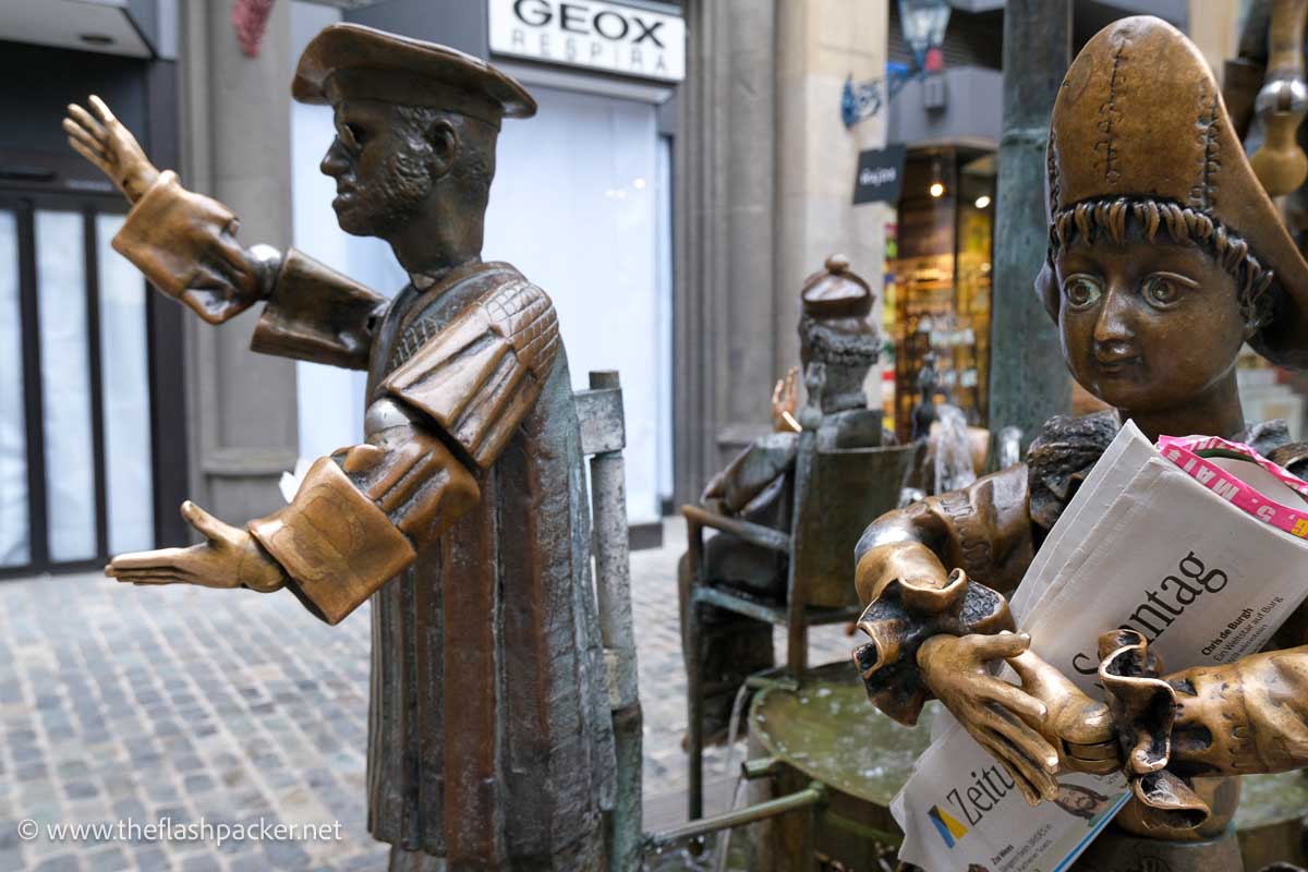 two bronze figures with one holding a newspaper