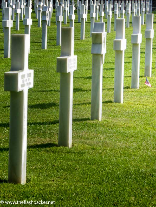 row of white crosse in war cemetery and a single small american flag