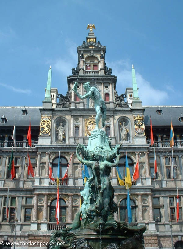 bronze statue in front of large half gabled building with flags