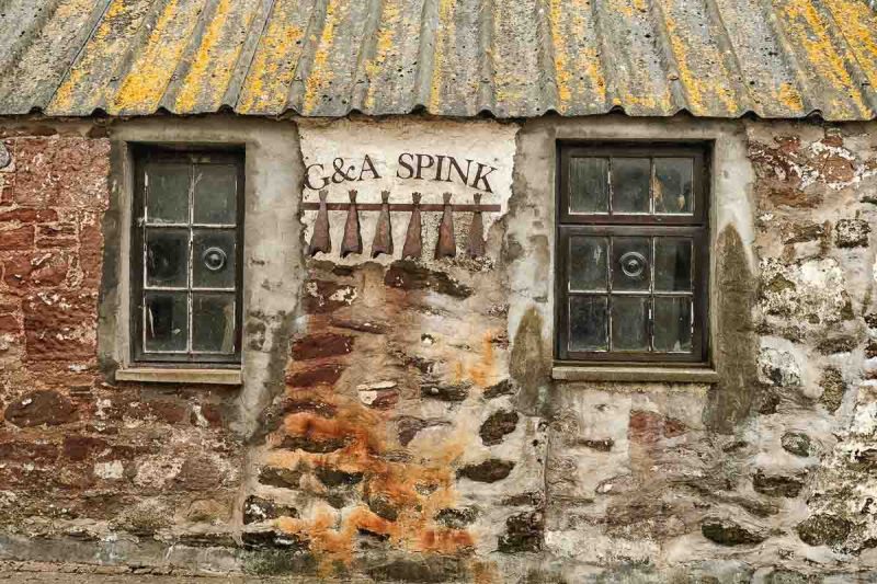 weathered exterior of stone building with metal sign with fish