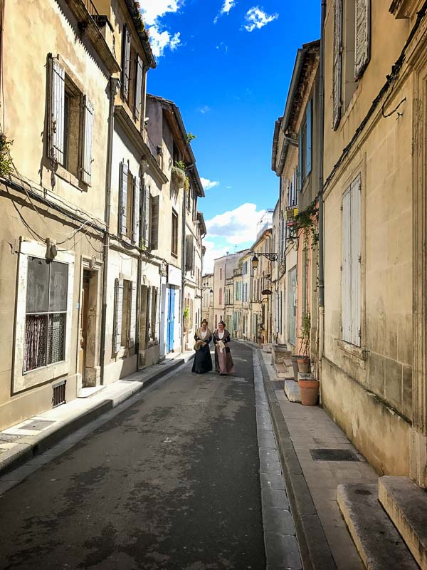 2 women in medieval costume walking along a narrow Arles street