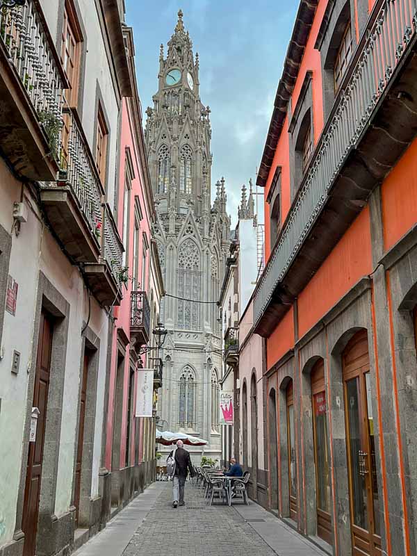 man walking down a narrow street towards the spire of a Gothic church