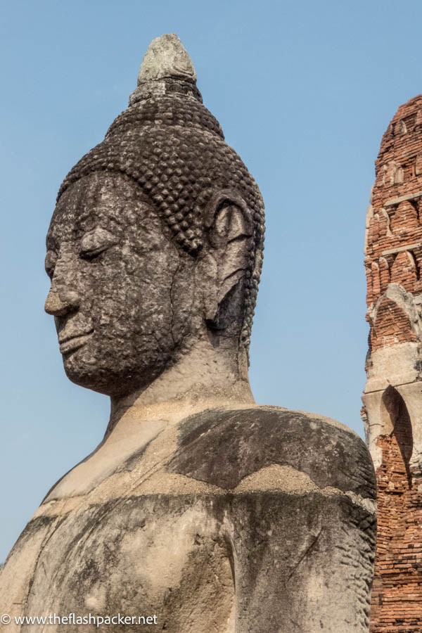 head of buddha with ruined temple buildings in background