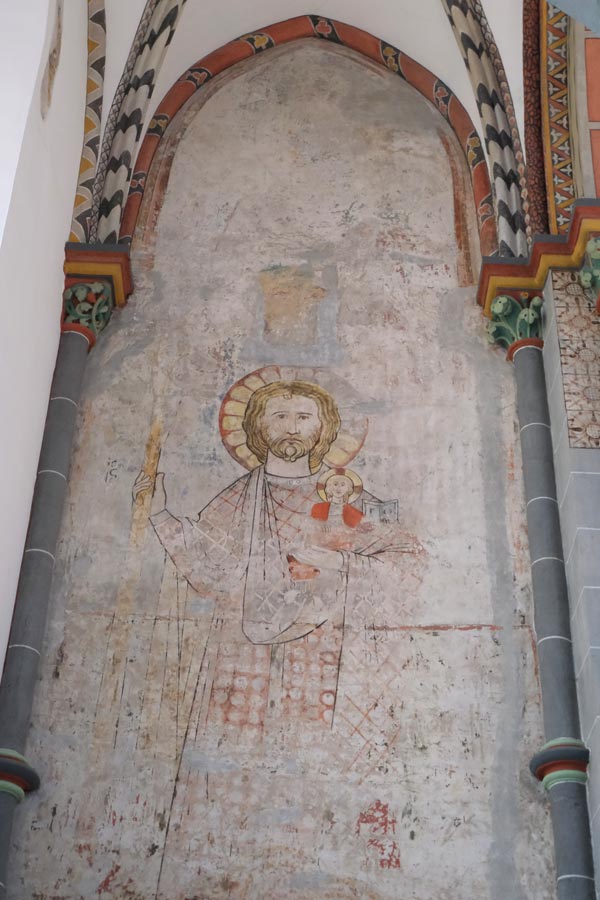 faded fresco of saint holding a child under a church arch