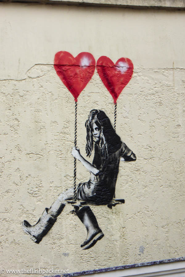 street art of girl on swing holding two red baloons