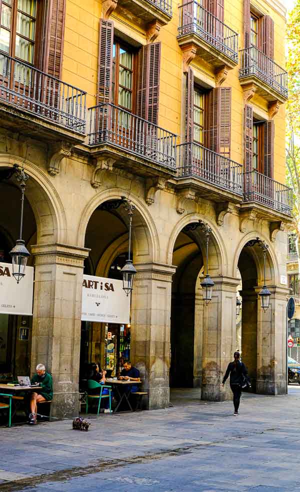 woman walking past ochre coloured colonnaded building in barcelona spain