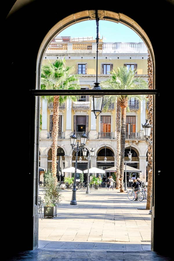 square with ornate lamposts and palm trees viewed through arch