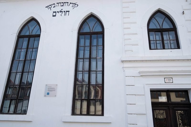 whitewashed exterior of synagogue with gothic type windows and hebrew lettering