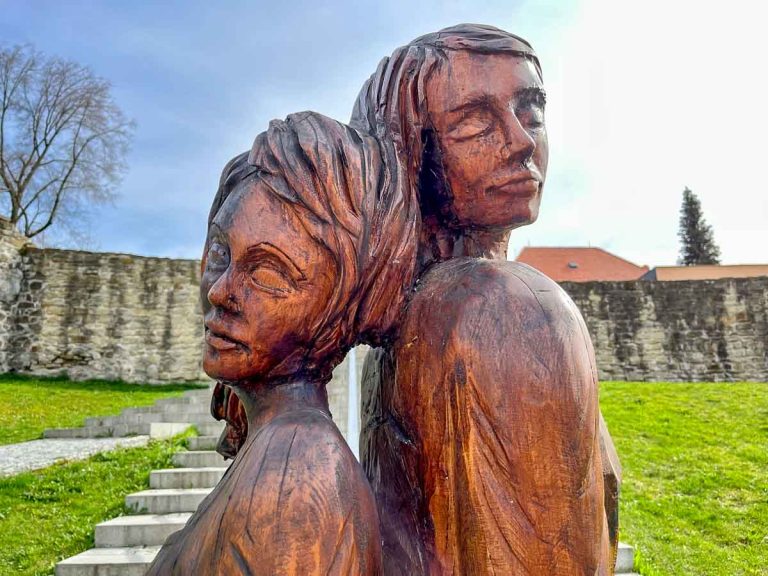 wooden sculpture of two women standing back to back