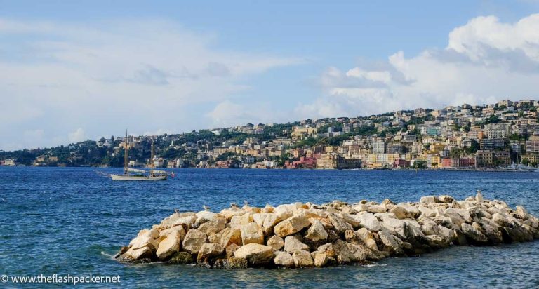 blue sea and sky with fishing boat and buildings lining shoreline seen during one day in naples