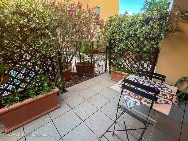 terrace of an apartment with pink and white flowers, a small table and 2 chairs