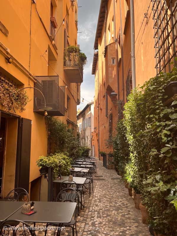 tables and chairs in a narrow lane lined with orange coloured buildings in bologna italy