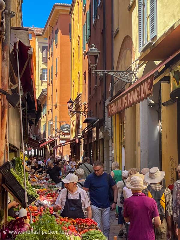 a narrow street in bologna lined with brightly coloured buildings and food stalls