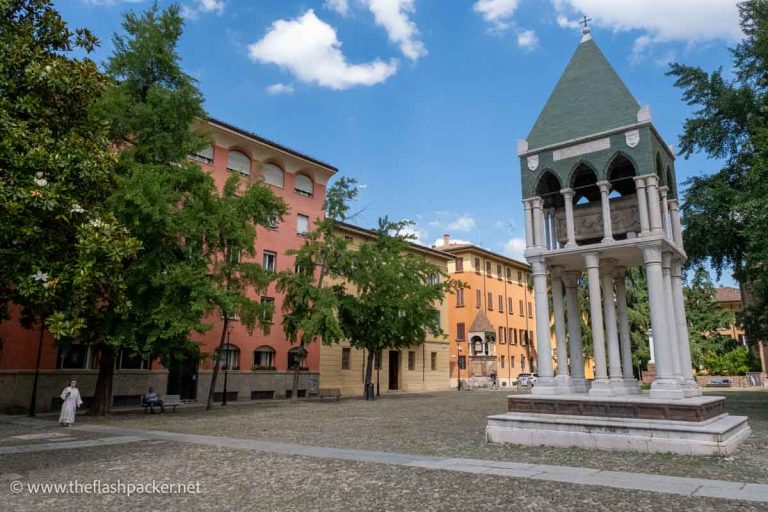 nun walking across a small piazza towards a central monument with a raised tomb