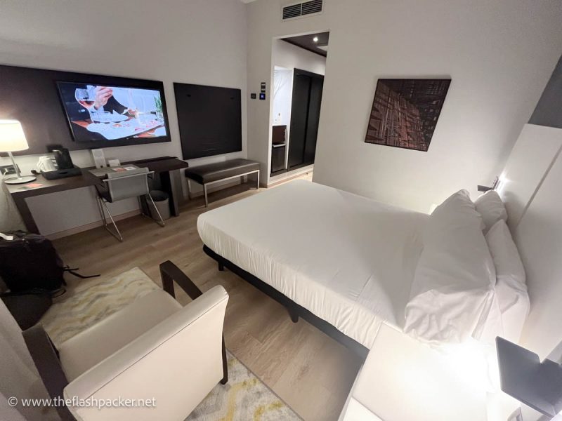 modern room at savhotel in bologna with bed with white linen, armchair and large tv