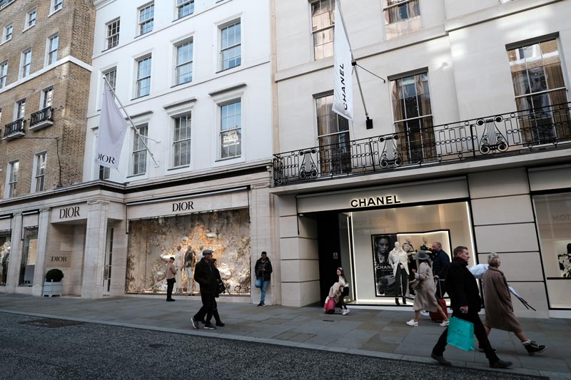 people walking past high end boutiques in a street in london