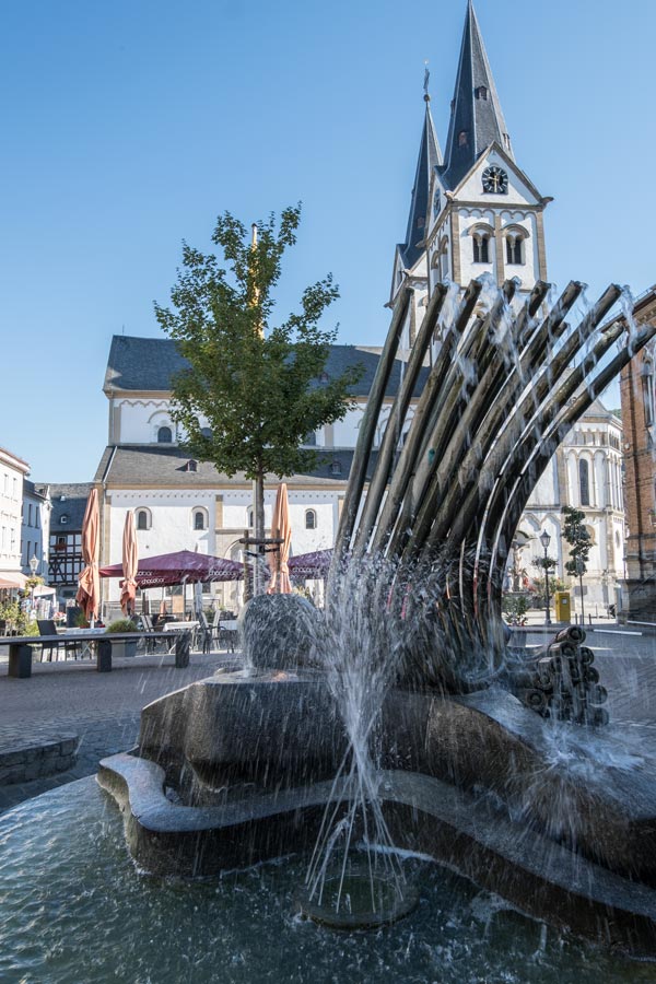 modern fountain in front of the main square in boppard bermany with large church with 2 bell towers