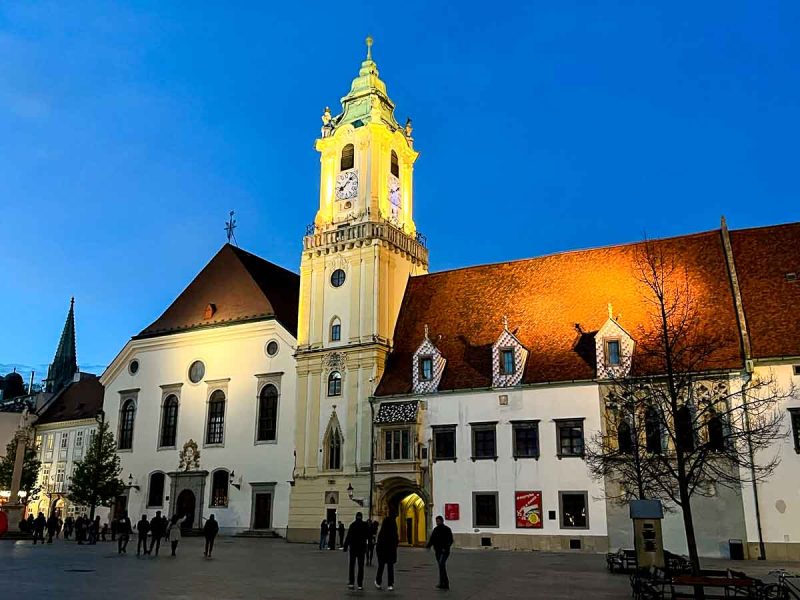 pretty illuminated old buildings with clock tower in square in bratislava at night