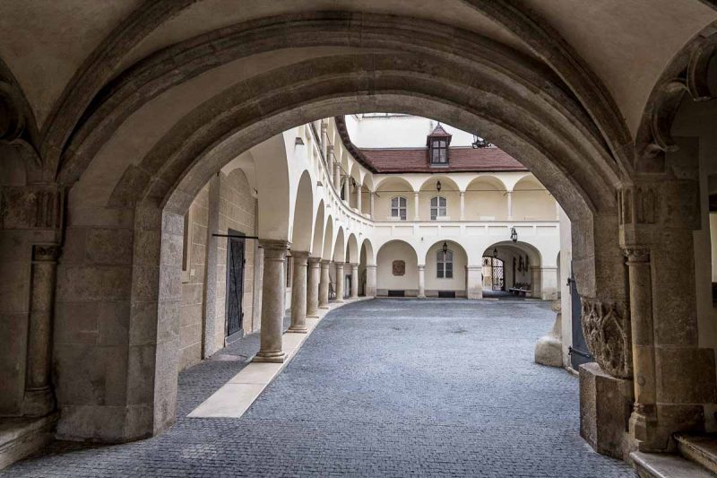 whitewashed colonnaded building of old town hall in bratislava viewed through an arch