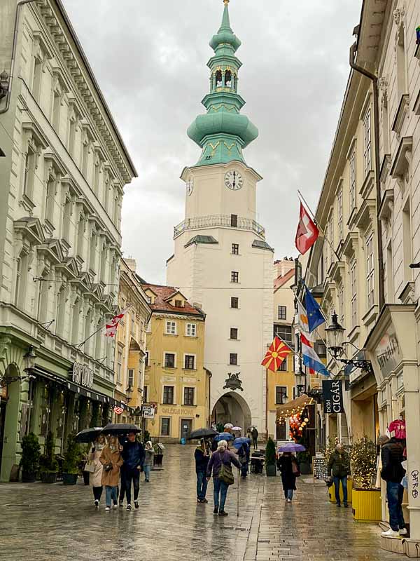 a gate topped with a large tower with an oinion domw at the end of a street in bratislava