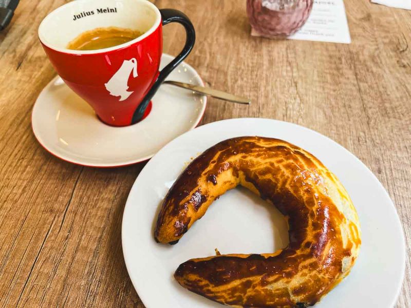 s-shaped sweet bagel on a white plate with a cup of coffee