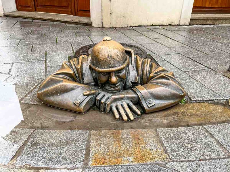 bronze sculpture of a workman coming out of a manhole cover