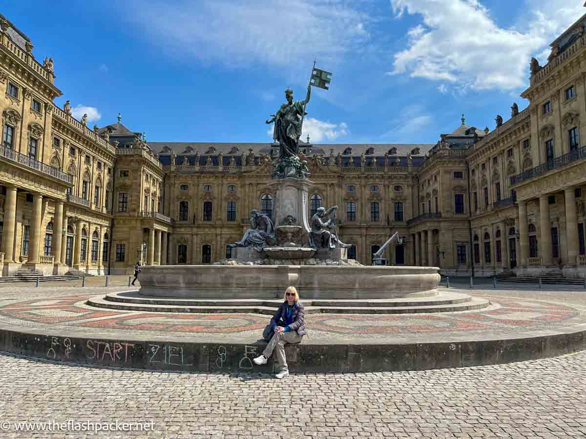 a woman sitting by a fountain in front of the wurzburg residence in germany