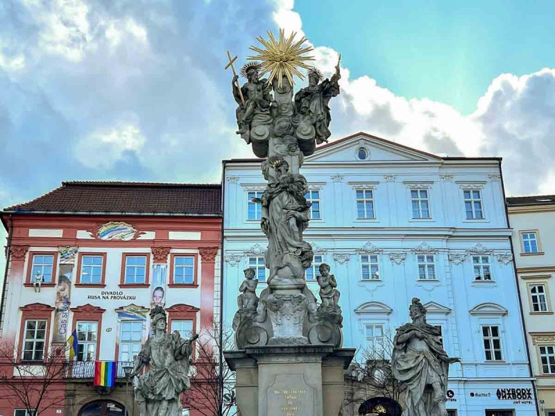 ornate baroque column in front of red and white medieval buildings in brno cabbage market