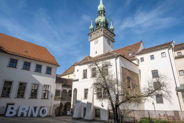 white buildings and a clock tower in a small square with a sign saying brno