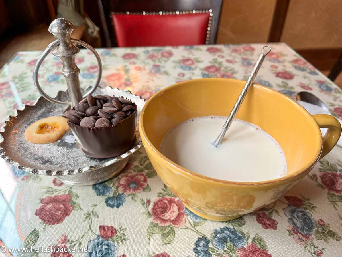 large yellow mug of milk with whisk and bowl of chocolate pellets