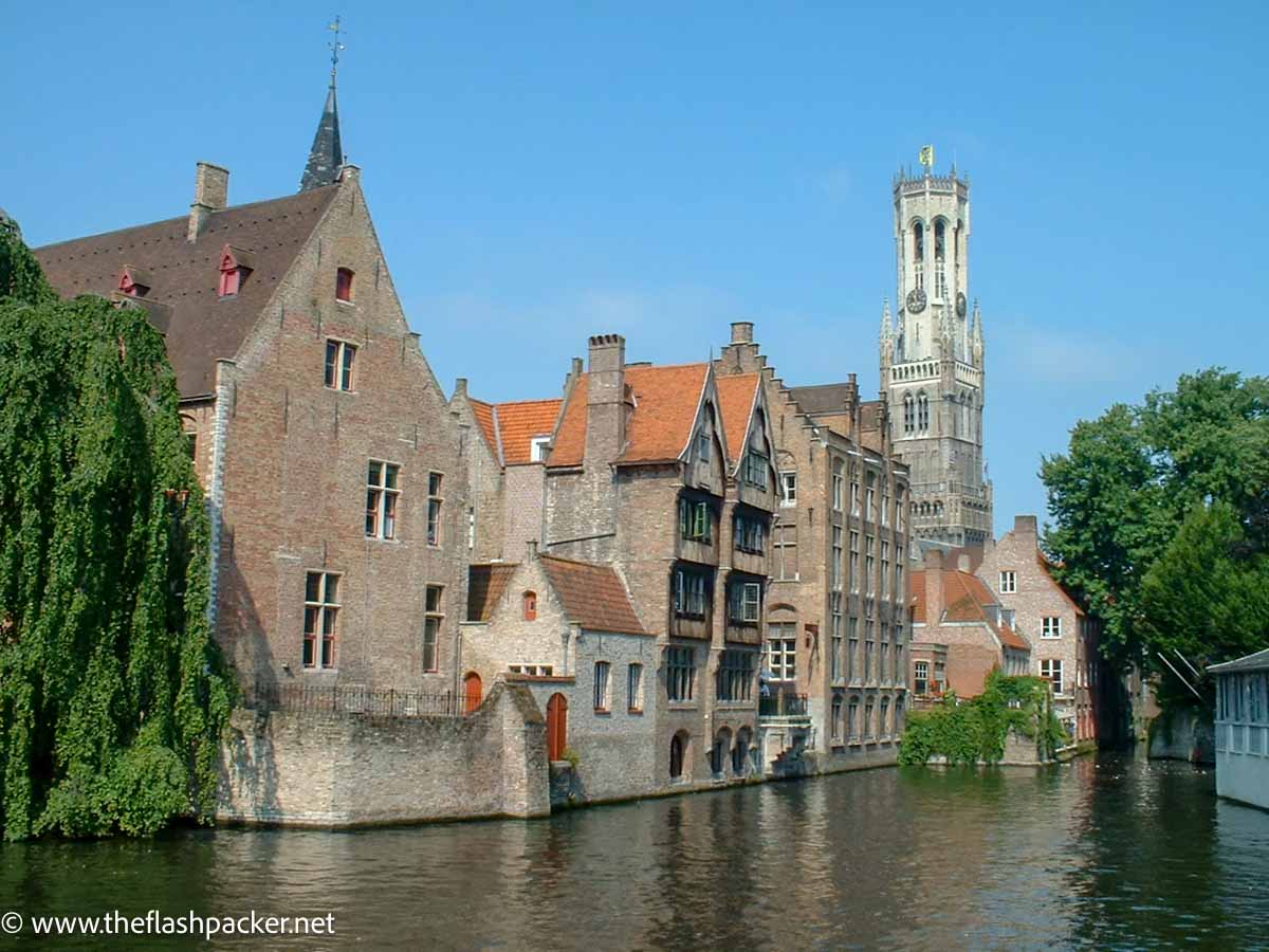 old houses and church steeple by side of river in bruges belgium