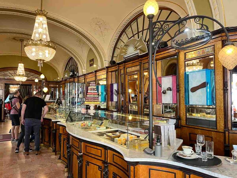 people standing at ornate counter of gerbeaud cafe in budapest