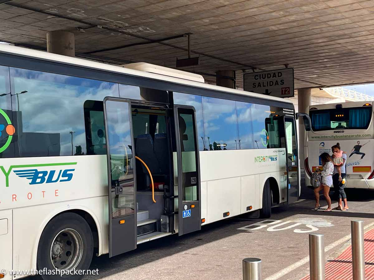 a family waiting by a large bus in front of an airport building in lanzarote