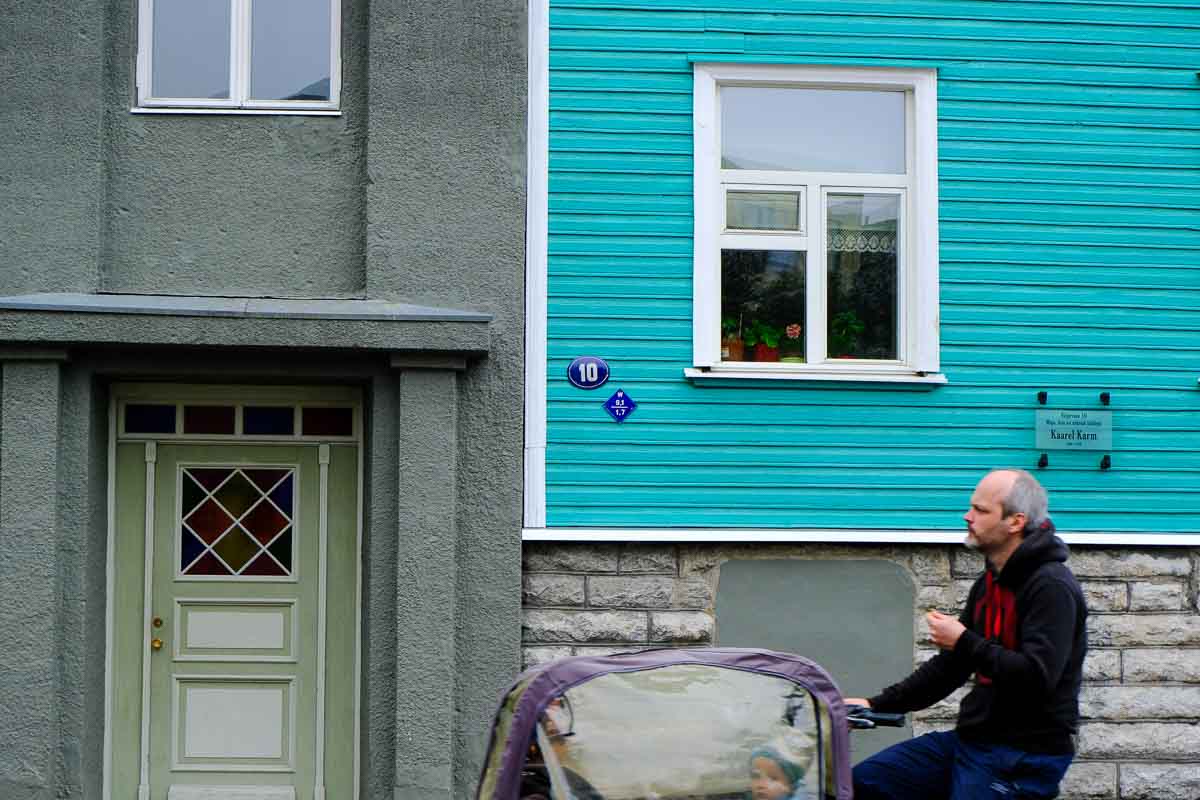 man riding bike with baby carrier past a teal coloured half timbered building