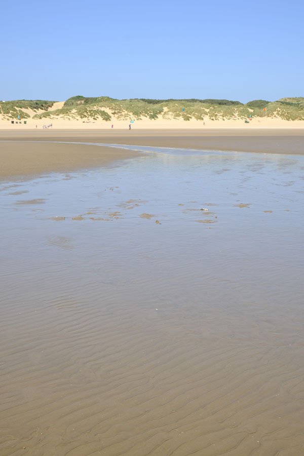 broad sand beach with tidal pool leading to grassy sand dune at camber sands beach