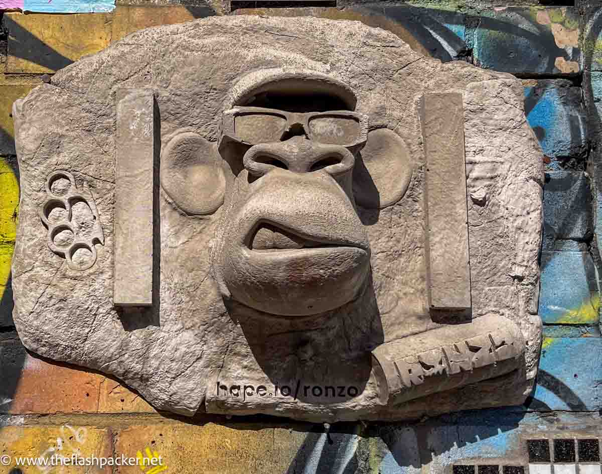 concrete wall sculpture of a face wearing spectacles and a cap